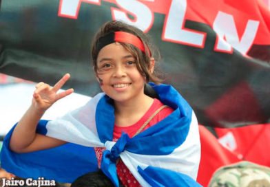 Jovencita saludando con la bandera de Nicaragua y el Frente Sandinista en su espalda