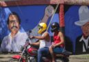 Motociclista y pasajero pasan frente a un mural de Sandino y el Comandante Daniel